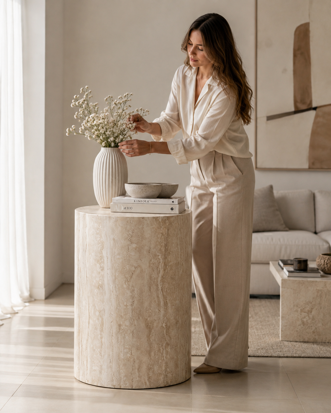ORLO cylindrical travertine side table by DEKATO LIVING with a woman arranging flowers in a contemporary living room