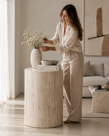 ORLO cylindrical travertine side table by DEKATO LIVING with a woman arranging flowers in a contemporary living room