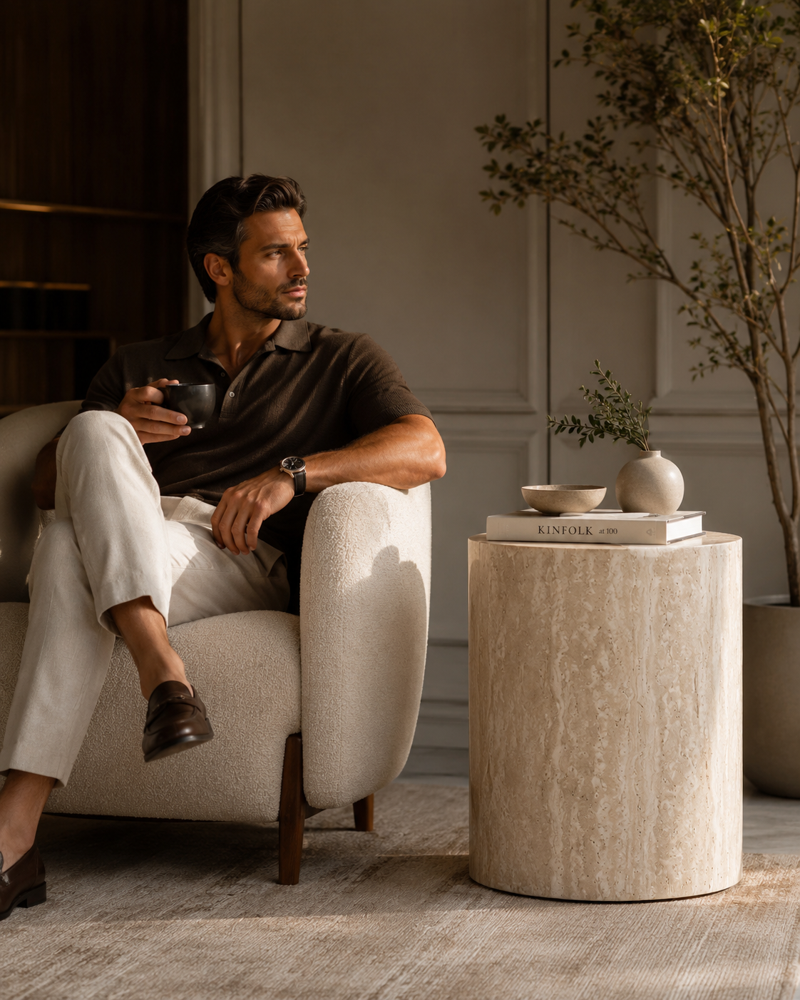 ORLO natural travertine pedestal side table by DEKATO LIVING beside a man relaxing with coffee in a warm living room