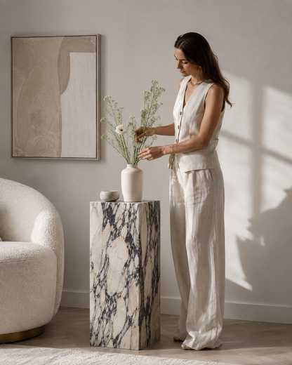 VIOLA Calacatta Viola marble pedestal by DEKATO LIVING with a woman arranging flowers in a refined neutral living room